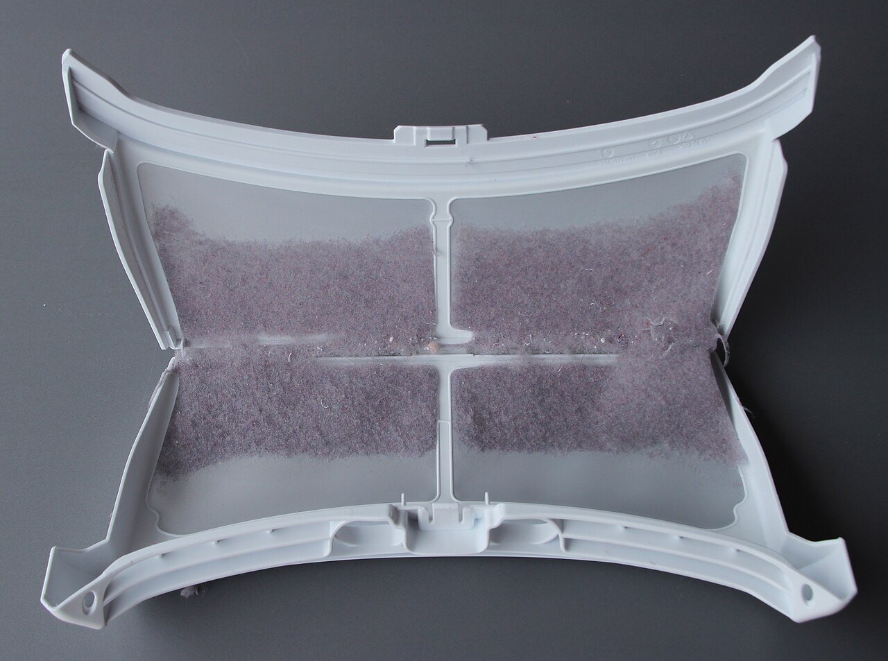 A white plastic tumble dryer lint filter opened flat, its mesh panels coated with a thick layer of gray-purple lint