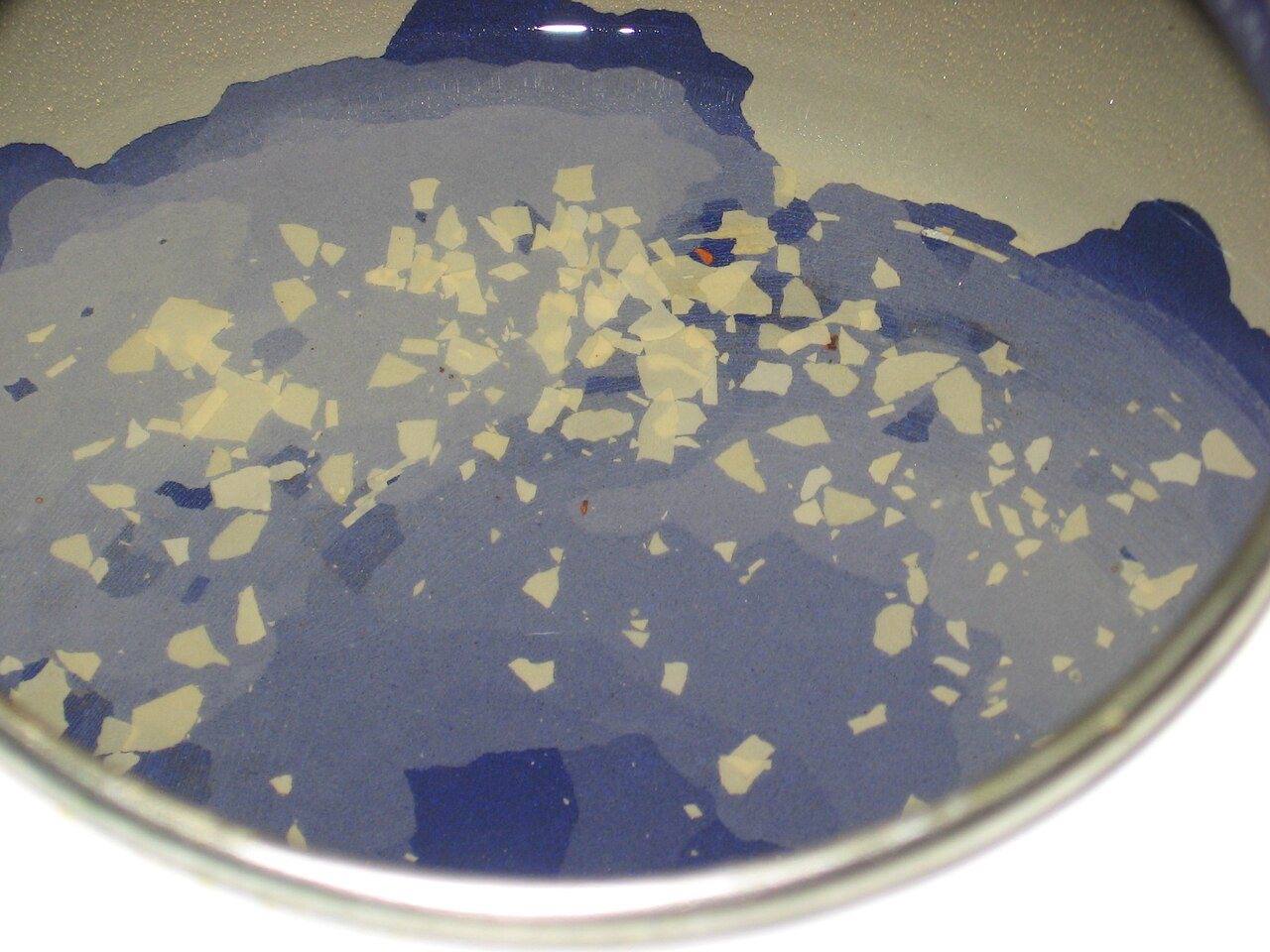 Flakes of white limescale floating in water inside a blue enamel pan
